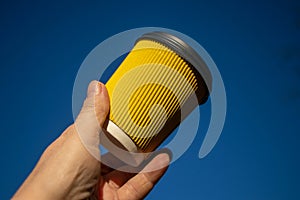 Corrugated yellow paper cup for coffee against a blue sky