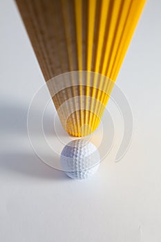 Corrugated yellow paper roll and golf ball on the white desk.