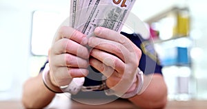 Corrupt policeman in handcuffs holds dollars in hand