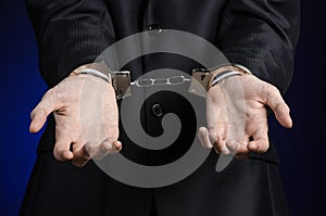 Corruption and bribery theme: businessman in a black suit with handcuffs on his hands on a dark blue background in studio isolated