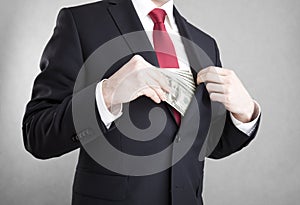 Corruption. Man putting money in suit jacket pocket.