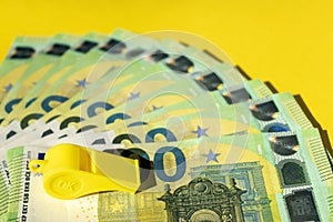 Corruption in sports or betting concept. Whistle and money on yellow background. Euro currency and referee whistle