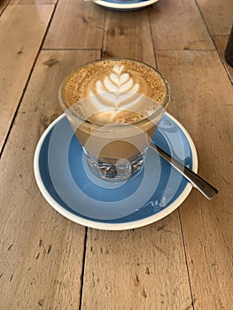 A cortado coffee in a glass on a blue saucer against a wooden background