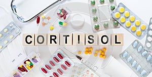 CORTISOL word made with wooden building blocks. Front view. CORTISOL text on white table with stethoscope and tablets background