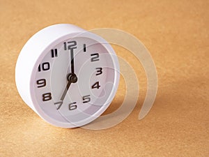 Cose up, white clock shows time at 7 o\'clock on the office brown workplace tabletop.