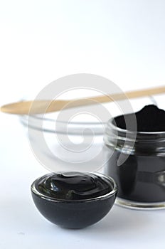 Cosmetic activated carbon charcoal powder in a glass jar and beauty face mask mixture on white with copy space.