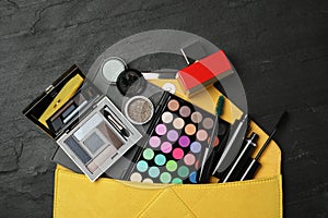 Cosmetic bag with makeup products on slate background, flat lay