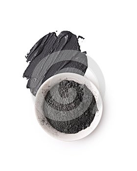 Cosmetic black clay powder in white ceramic bowl with a smear