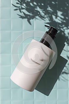 Cosmetic body lotion bottle on blue paper checkered texture background on the sunlight with leaves shadow.