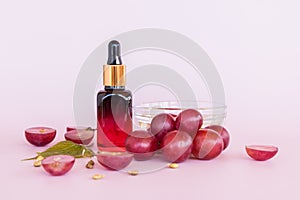 cosmetic bottle with a colored glass pipette with organic oil or grape seed face serum. pink background with a bunch of