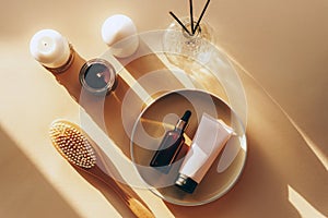 Cosmetic bottle and cream tube on a plate with natural wooden body brush and candles on a light background. Natural