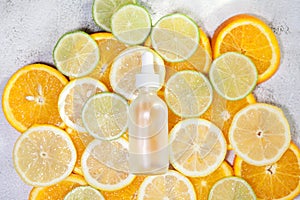 Cosmetic bottle made of transparent glass with pipette on fresh lemon, orange, lime slices background. Copy space