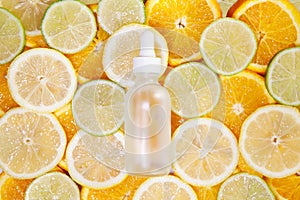 Cosmetic bottle made of transparent glass with pipette on fresh lemon, orange, lime slices background. Copy space