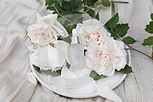 Cosmetic bottle, perfume. Rose water, essential oil. Roses flowers on beige linen table cloth background. Pink glass