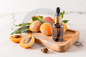cosmetic bottle with a pipette with moisturizing serum or apricot kernel oil on wooden tray among ripe apricots. a