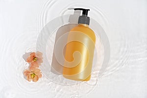 Cosmetic bottle on white background with water and flowers. Top view, closeup.