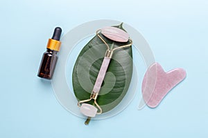 Cosmetic bottles, face serum, facial massage roller and Gua Sha massager on blue background. Anti age, lifting and toning photo