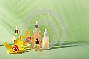 Cosmetic care products in glass bottles with orchid flowers - serums, cream, gel, oils. Concept for face and body care