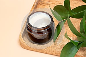 Cosmetic cream with fresh green ruskus leaves on wooden tray on beige background. Dermatologic, components for cosmetics