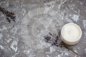 Cosmetic cream and lavender flowers on a gray background.