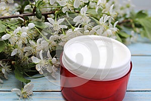 Cosmetic cream in a red container on the background of cherry flowers