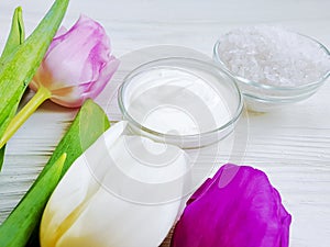 cosmetic cream, salt, tulip flower on a white wooden background