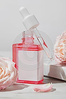Cosmetic dropper bottle with rose extract. Serum for face skin with rose extract in a glass bottle with a pipette and pink roses