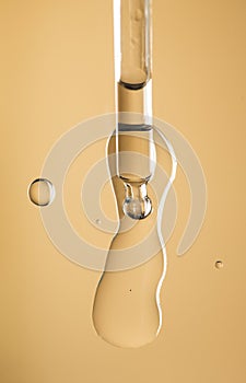 Cosmetic dropper with serum, beauty cosmetics dripping, on beige background. Macro shot