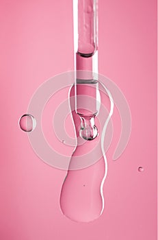 Cosmetic dropper with serum, beauty cosmetics dripping, on pink background. Macro shot