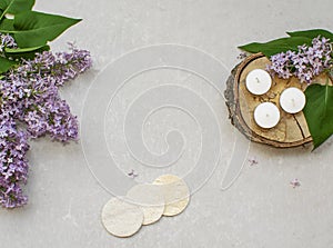 Cosmetic flat lay with a bouquet flowers lilac.Spa set of natural sponges and candles on wooden slice on grey backgr