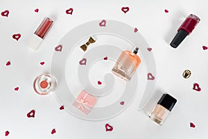 Cosmetic flat lay - perfume, nail polish, lipstick, small gift box, golden accessories on white background with tiny red hearts am