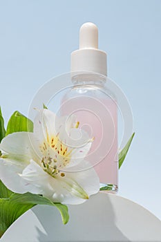 Cosmetic glass bottle with dropper on podium with alstromeria flowers. The concept of a beauty salon and natural