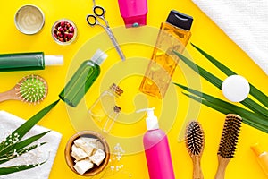 Cosmetic for hair treatment with shampoo, styling, oil, comb, scissors on yellow background top view pattern