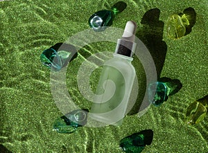 Cosmetic hydrating serum in a glass bottle with pipette close up. Hyaluronic acid on the green background top view with