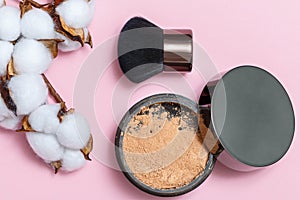 Cosmetic loose powder for face makeup in an open jar with a brush and a branch of cotton on a pink background