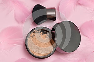 Cosmetic loose powder for face makeup in an open jar with a brush on a pink background