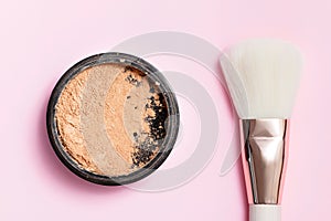 Cosmetic loose powder for face makeup in an open jar with a face brush on a pink background