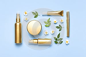 Cosmetic mock up gold bottles. Cosmetics, spring white flowers green leaves on blue background. Cosmetics springtime summer