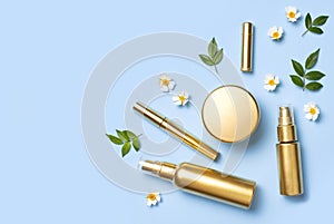 Cosmetic mock up gold bottles. Cosmetics, spring white flowers green leaves on blue background. Cosmetics springtime summer