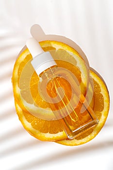 Cosmetic organic, vitamin C extract. Slices of orange and serum dropper bottle on white background with palm shadow, top