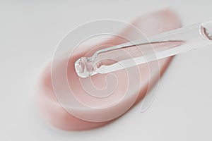 Cosmetic pipette with drops of oil, on the background of cosmetic cream smear