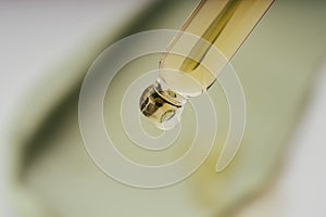 Cosmetic pipette with drops of oil, on the background of green cosmetic cream smear