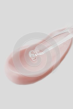 Cosmetic pipette with drops of oil, on the background of pink cosmetic cream smear