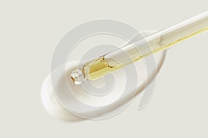 Cosmetic pipette with drops of oil, on the background of white cosmetic cream smear