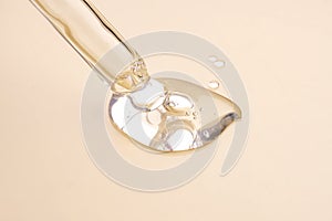 A cosmetic product gel or collagen serum flows out of a pipette with bubbles on beige background