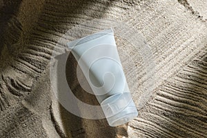 Cosmetic product in tube on nature background with sand. Essential cream for moisturizing body skin, face care, sunblock. mockup