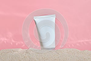 Cosmetic product in tube on pink background with sand. Essential cream for moisturizing body skin, face care, sunblock. mockup of