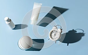 Cosmetic products and an alarm clock levitate over a blue background. The concept of anti-aging cosmetics