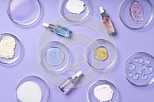 Cosmetic products, scrub, face serum and gel in many petri dishes on a violet background. Cosmetics laboratory research