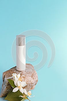 Cosmetic serum bottle in white blank package on the stone with jasmine blossom, blue background